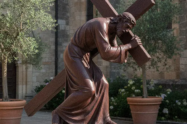 Full round bronze statue of Jesus carrying the cross for prayer garden