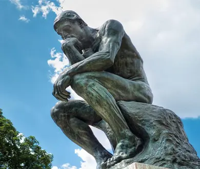 Side view of bronze Thinker statue against blue sky