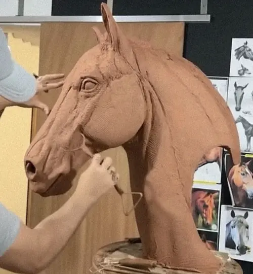 Artist sculpting clay model of horse head for custom bronze casting