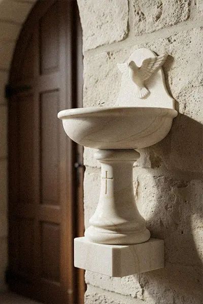 Small white marble holy water stoup mounted on stone wall