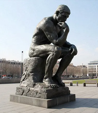 Life-size bronze Rodin Thinker statue sitting on a rock base