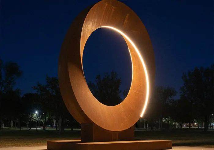 Illuminated corten steel moon gate sculpture with LED lights at night