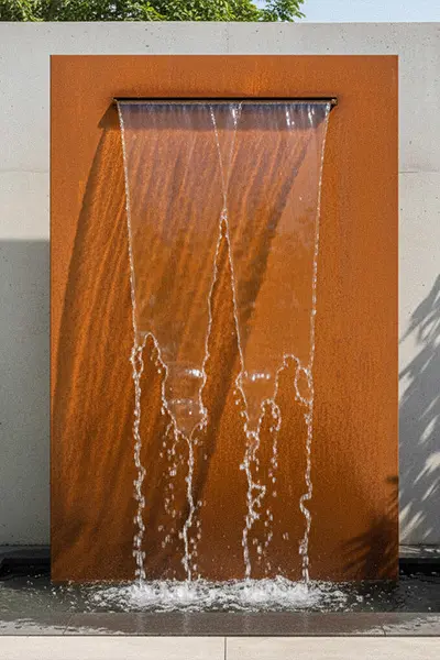 Rusty metal wall water feature with water flowing down surface