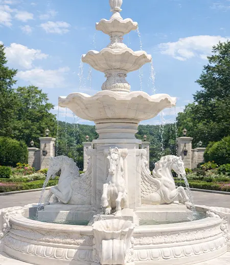 Large white marble tiered fountain with horse statues in pool