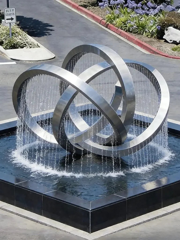 A large mirror-finished stainless steel fountain with an infinite loop design flows water within a park.