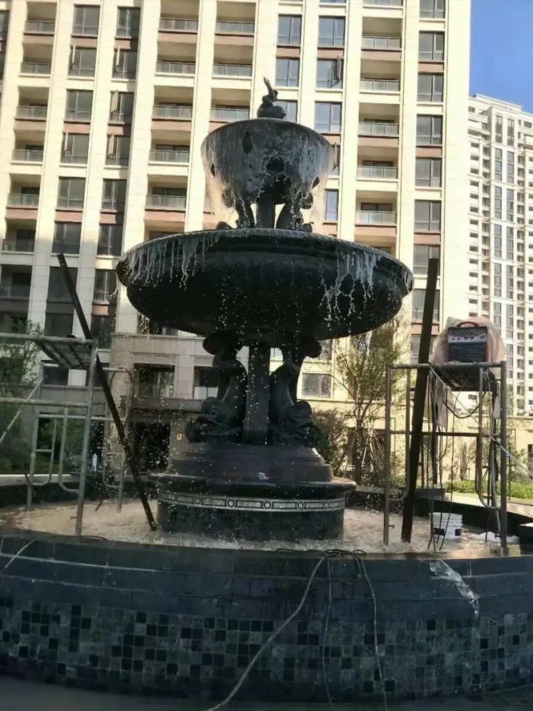 Final water flow test of a newly installed classic 3-tier bronze fountain, showcasing the cascading water effect in a completed outdoor garden landscape.