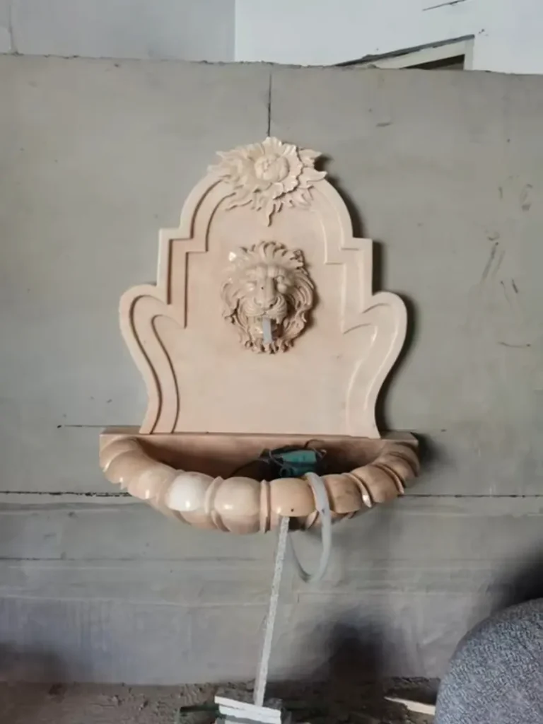 Marble lion head wall fountain during installation with integrated water outlet and wall-mounted basin.