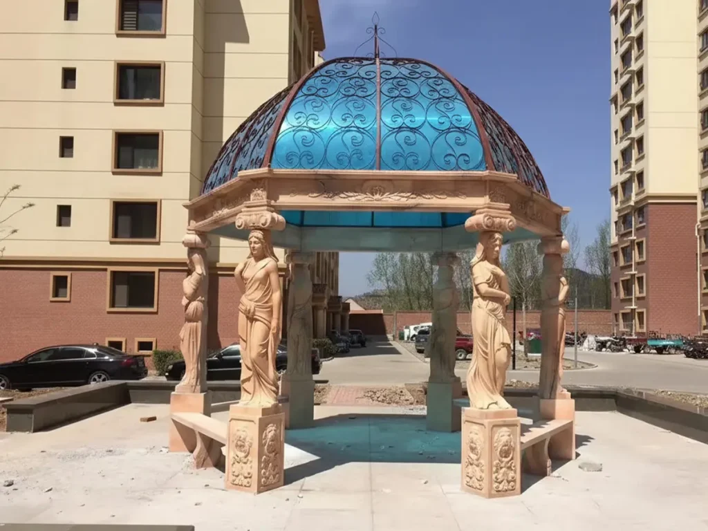 Fully completed red marble gazebo with caryatid columns and wrought iron dome in a luxury landscaped garden setting.