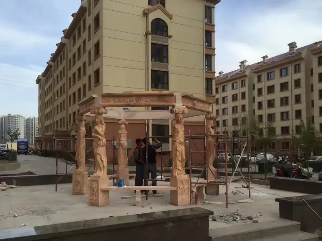 Workers assembling the upper structure of a hand-carved marble gazebo during on-site installation.