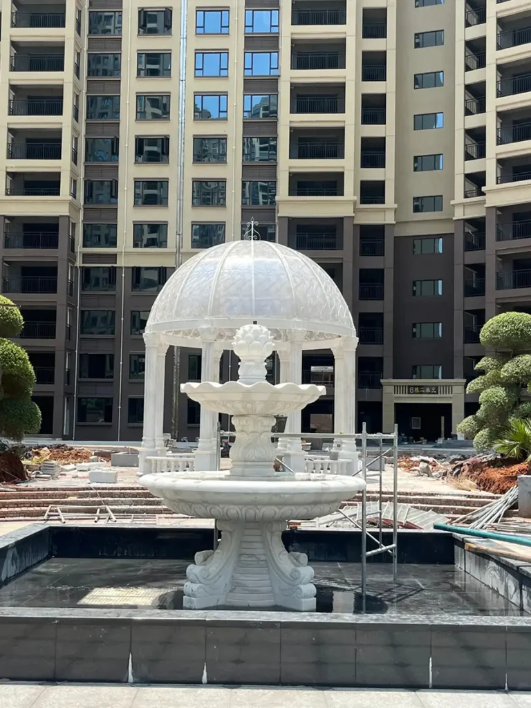 White marble gazebo with matching marble fountain installed in luxury estate garden during daytime showing completed custom garden architecture project