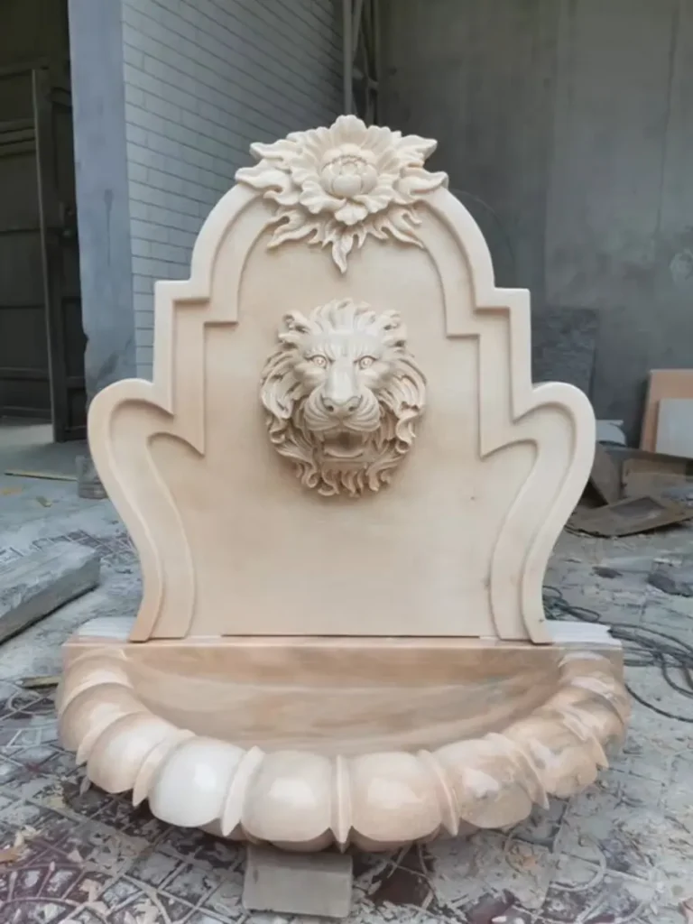Classic marble lion head wall fountain with scalloped shell basin and ornamental carved backplate.
