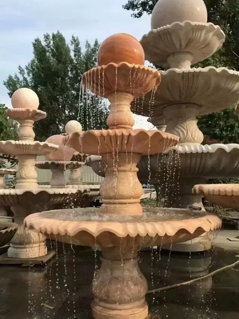 Three-tier marble garden fountain with carved scalloped bowls and stone ball finial, water cascading elegantly in outdoor display setting.