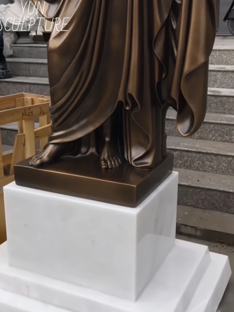 The base of a 180cm tall bronze Jesus statue secured on a white marble pedestal for church altar installations.