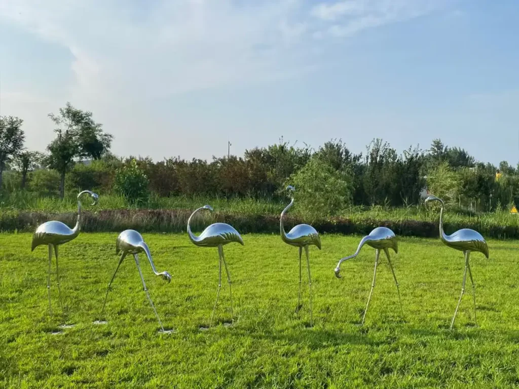 A flock of elegant flamingo outdoor metal animal sculptures placed across a wide green lawn. Crafted from highly durable 316L Marine Grade stainless steel, these weather-resistant pieces are perfectly engineered to survive harsh coastal environments while maintaining a brilliant, reflective surface.