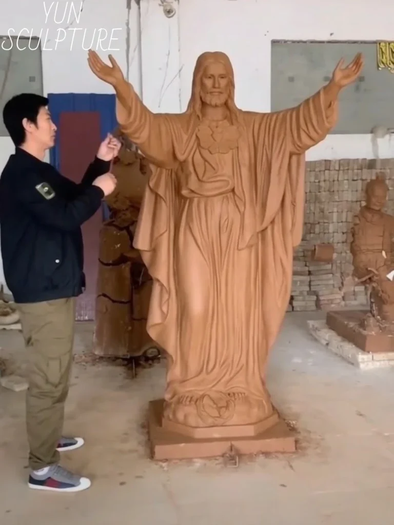A master sculptor standing beside a massive 1:1 clay original of a Jesus statue, carefully inspecting and refining the precise quality of the facial expression. This hands-on, human-guided process is the soul of the statue, ensuring the final bronze artwork communicates profound theological triumph across a 50-meter open courtyard.
