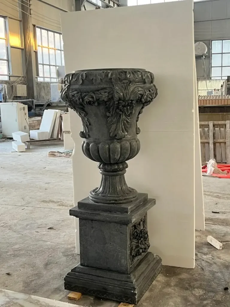 A handcrafted black granite garden urn and planter on a pedestal, showcased in a professional stone carving workshop before final installation.