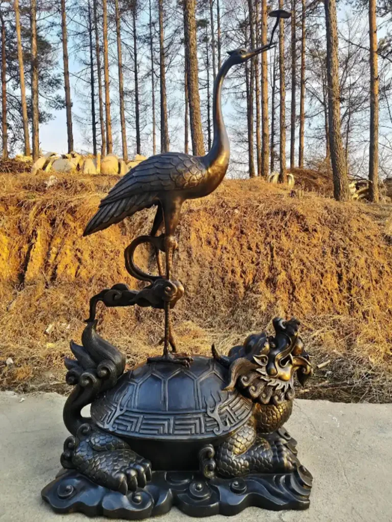 A traditional dark bronze crane sculpture standing elegantly on the back of a mythical dragon-turtle. In East Asian culture, this powerful combination symbolizes ultimate longevity, wisdom, and peace, making it a profound artistic centerpiece for oriental gardens.