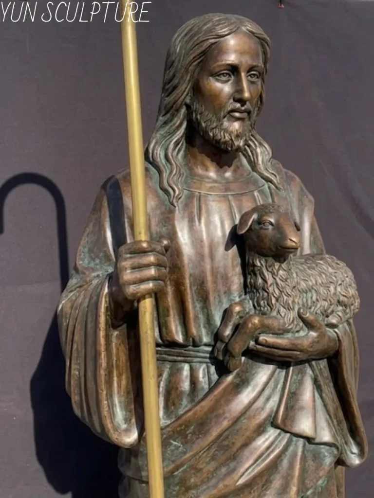 A full-body bronze Jesus statue of the Good Shepherd holding a staff and a lamb, with an antique patina finish, showcasing the intricate details of the sculpture.