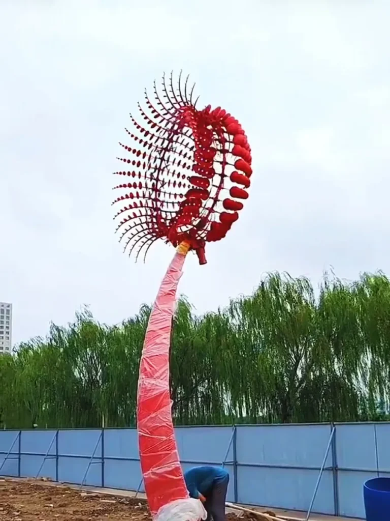 Professional installation of a large kinetic wind sculpture for sale, showing the assembly of the reinforced internal structural skeleton on a curved pole.