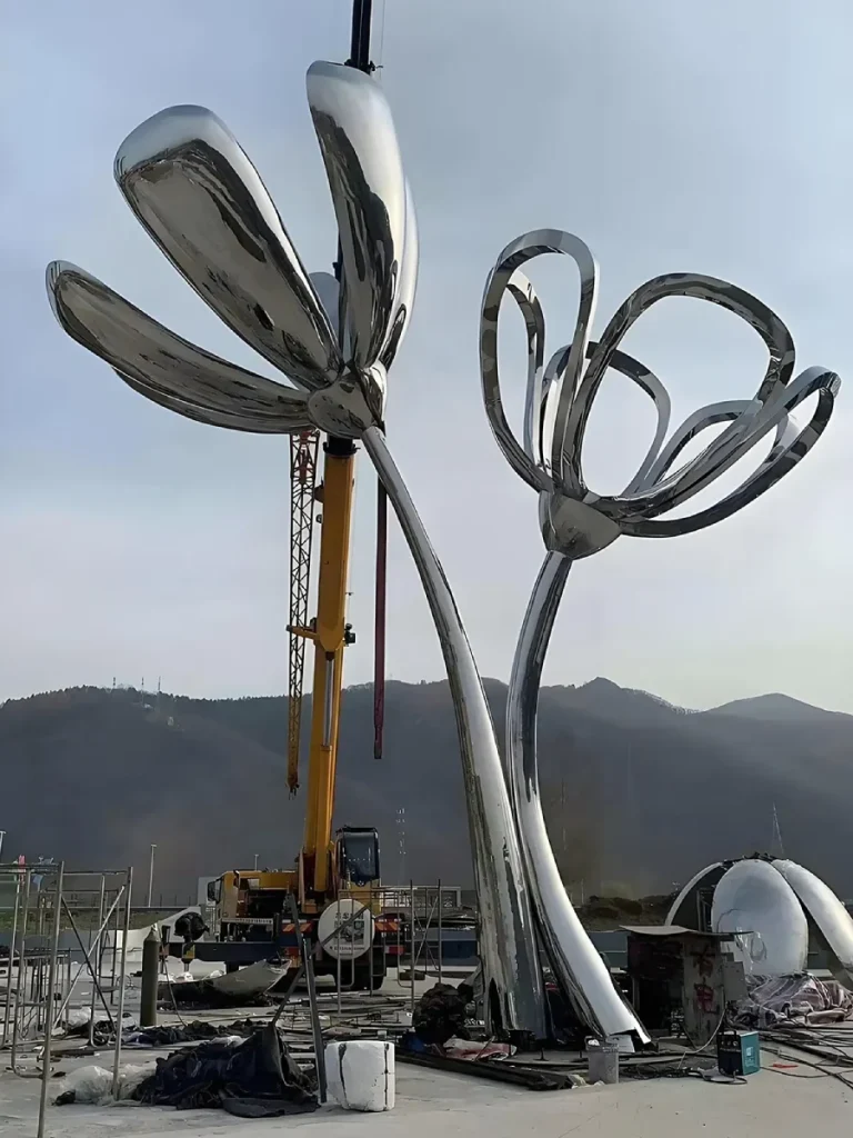 A low-angle view of an enormous stainless steel botanical sculpture during installation. This image visually supports our guide on buying stainless steel sculptures for modern home exteriors, proving that while the graceful curves appear effortless, their longevity is entirely determined by the invisible, heavy-duty internal framework hidden inside.