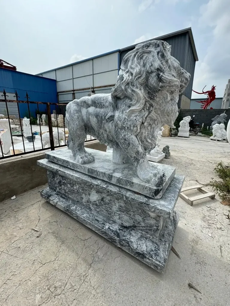 Rear-diagonal view of the standing grey marble lion on its thick stone base. The sculpture beautifully showcases the dramatic, flowing natural veins of the marble, highlighting the authentic craftsmanship that separates true stone art from cheap cast replicas.
