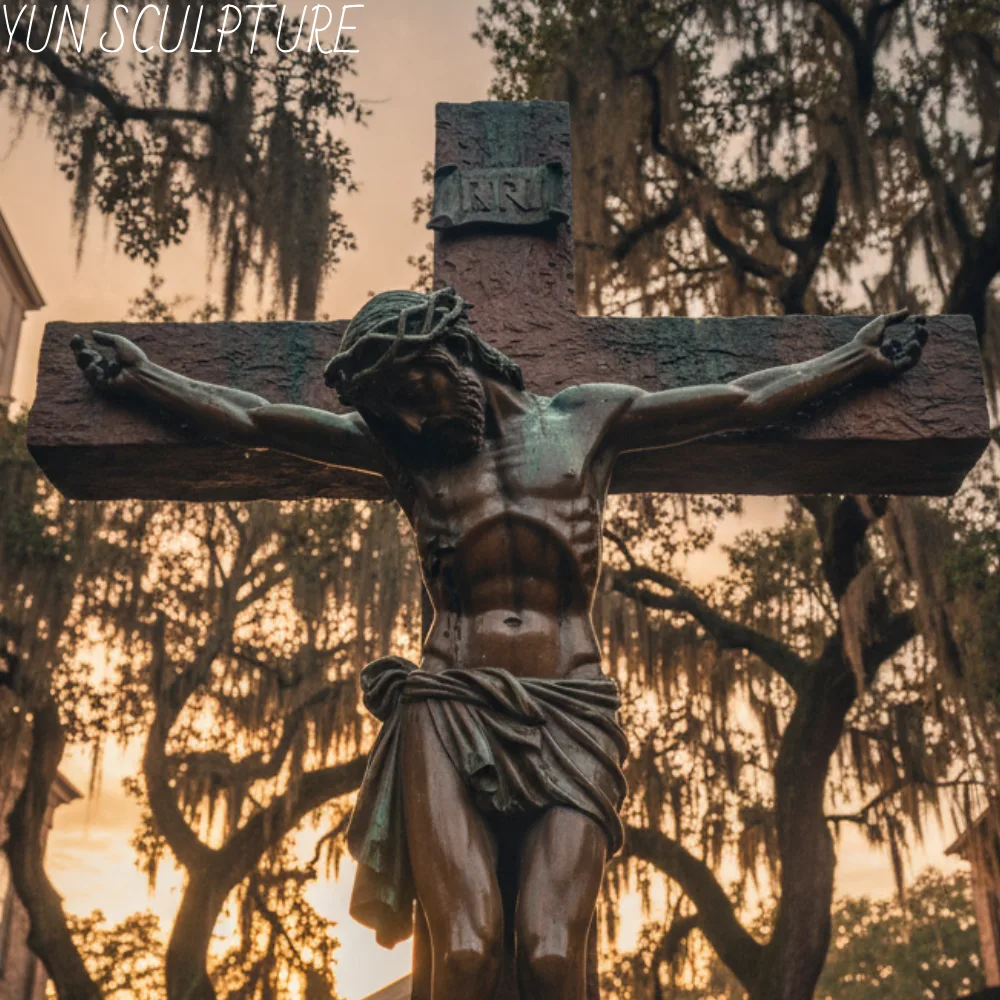 A monumental bronze crucified jesus statue standing solemnly against a dramatic sunset sky framed by ancient trees with Spanish moss. Depicting the traditional "Christus Patiens" form with a sagging body and closed eyes, this majestic sculpture perfectly aligns with the clear ecclesial preferences of Roman Catholic dioceses across the United States.