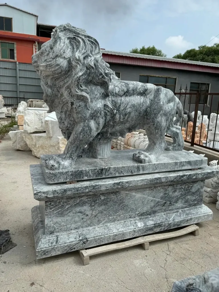 Side profile of a classical standing lion statue carved from grey marble, complete with a sturdy built-in pedestal. This highly detailed natural stone sculpture offers the softer, classical aesthetic favored by luxury estates, ensuring durability over centuries.
