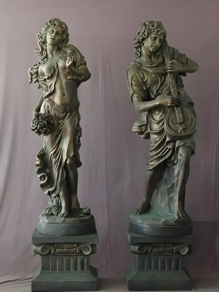 A pair of elegant classical female copper sculptures standing on ornate pedestals, beautifully showcasing a living surface of deep metallic glow and warm bronze tones. Unlike the static precision of stainless steel, these figures perfectly embody the "breathing copper" concept, introducing warmth and a natural verdigris patina that gracefully matures alongside historic districts and stone façades.