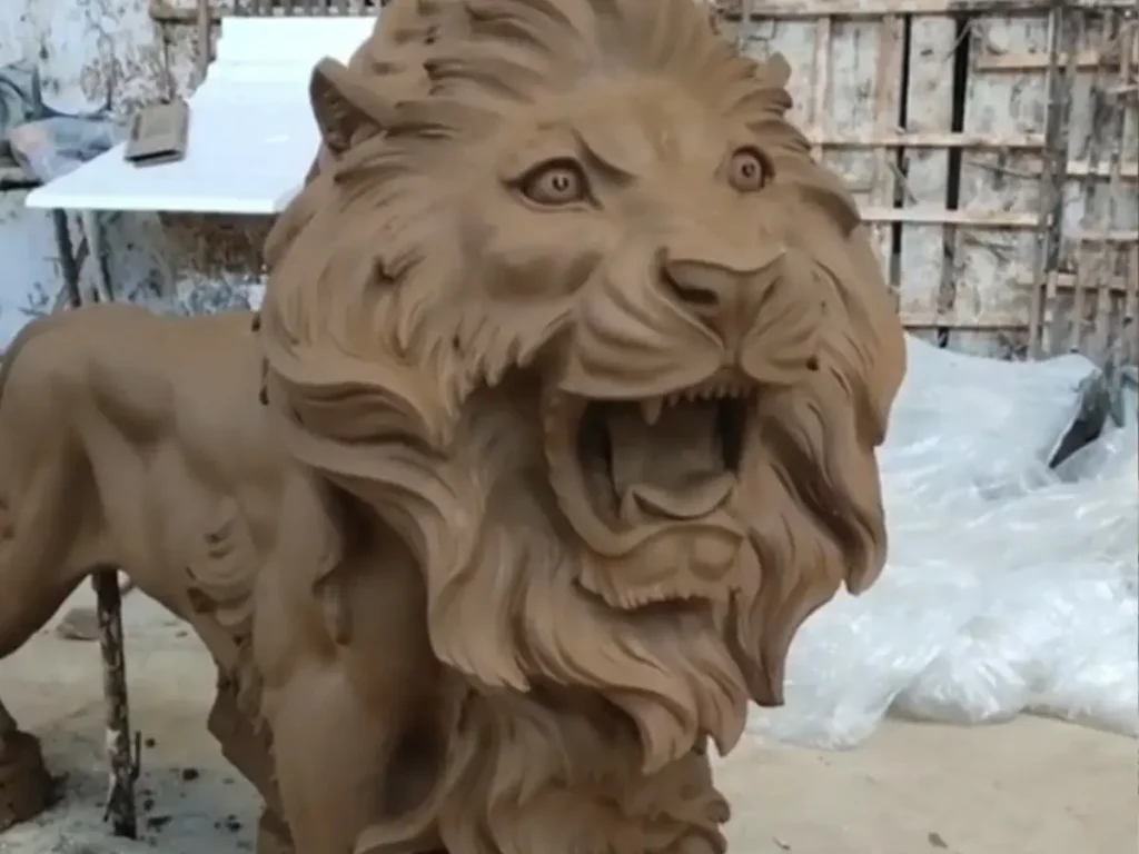 Detailed front-angle close-up of a roaring lion clay model in a workshop. The deep carving of the fierce facial expression demonstrates how master sculptors capture extremely subtle anatomical details before the traditional bronze mold is created.