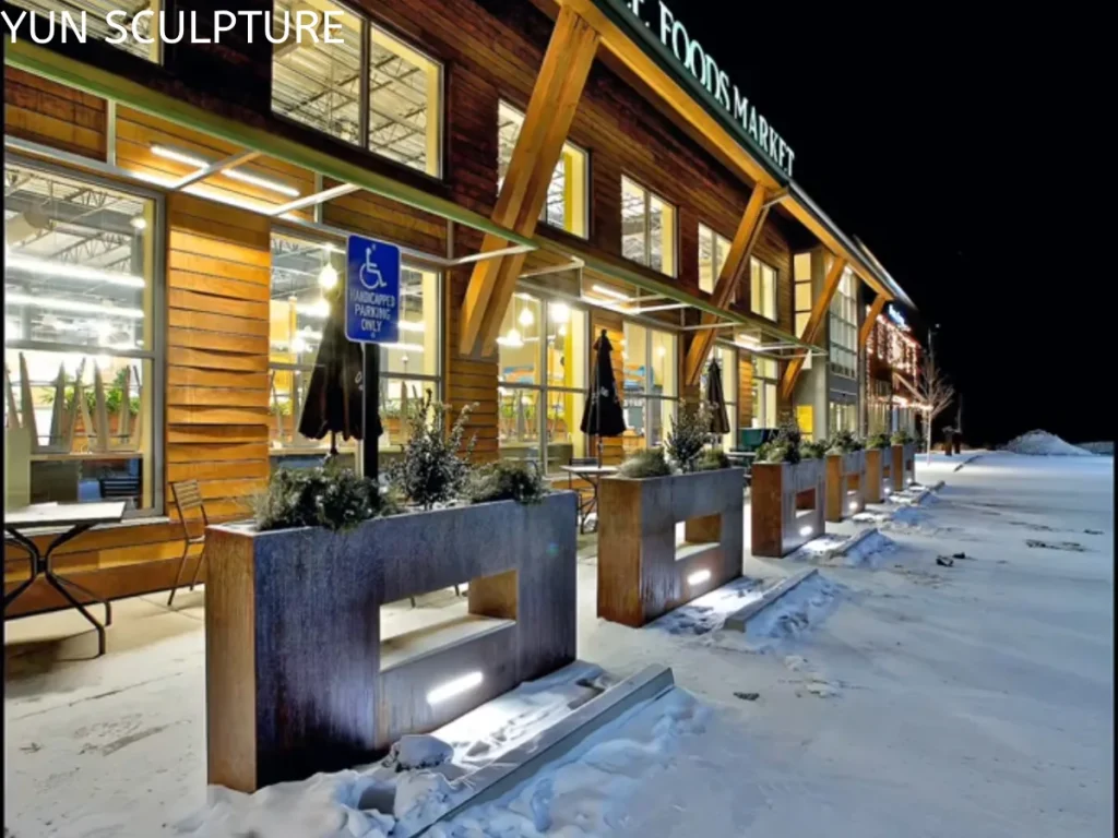 Large Corten steel planters with integrated lighting installed in a snowy commercial plaza, illustrating structural anchoring in exposed outdoor environments.