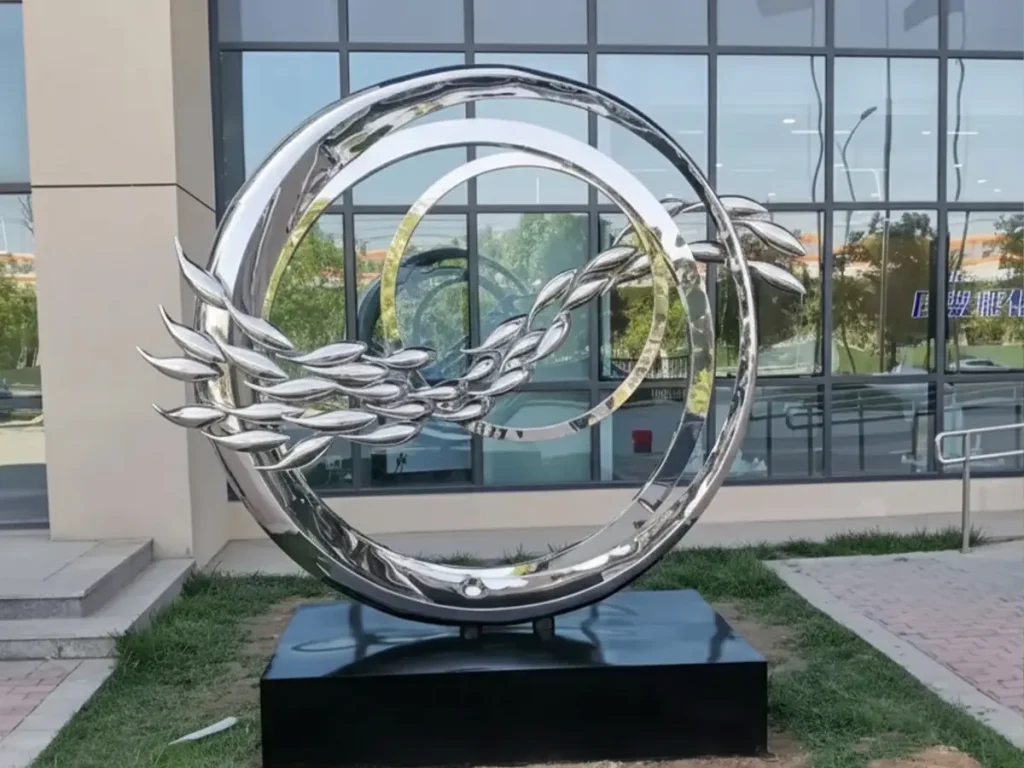 A contemporary metal sculpture featuring a school of sleek, stylized fish swimming through intersecting stainless steel rings. Mounted on a black stone base, this dynamic ocean-themed artwork seamlessly integrates architectural geometry with natural aquatic energy.