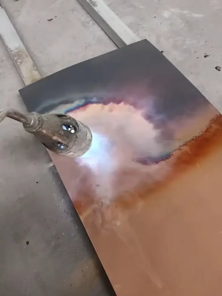 Heating a solid copper sheet with a torch for the initial annealing process in custom metal sculpture fabrication.
