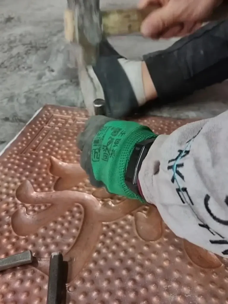 An artisan hammering the reverse side of a copper sheet to create 3D depth, a technique known as repoussé.