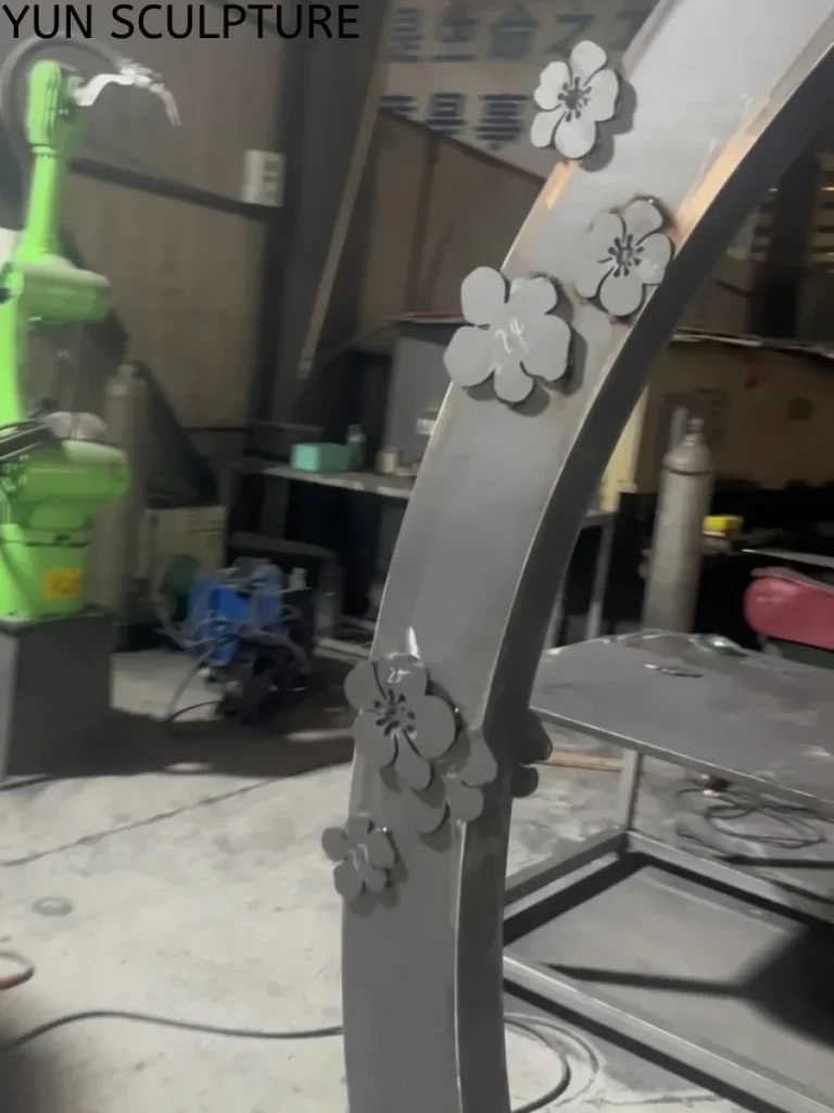 Close-up of laser-cut floral patterns on a raw metal moon gate frame during the manufacturing stage, showing the clean silver-grey surface of unweathered ASTM A588 steel.