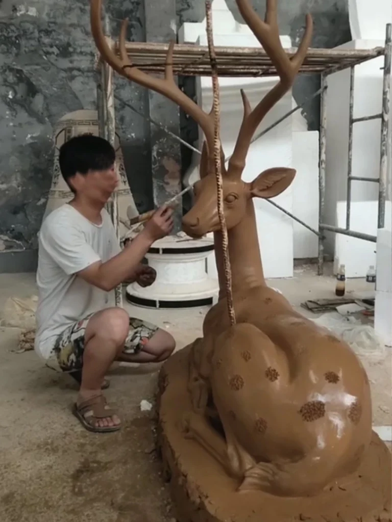 An artist carefully measuring and carving the clay prototype of a deer sculpture. Working with clay is crucial for perfecting the elegant angle of the neck and realistic body proportions, ensuring the final hollow bronze statue retains every handcrafted detail.
