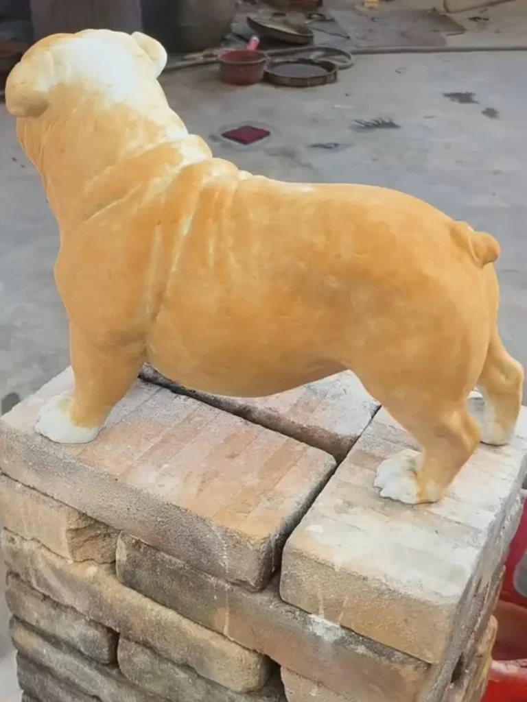 Rear view of a life-size bronze bulldog sculpture during the chemical coloring stage, showing the rich golden-brown finish achieved by hand.