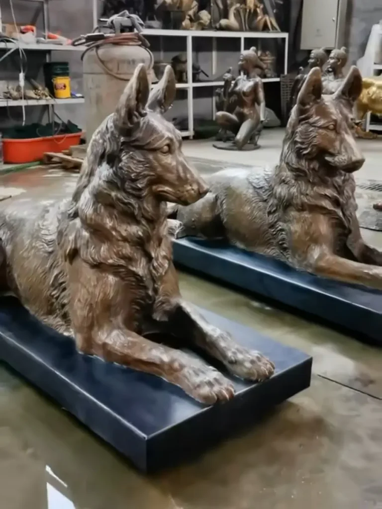 Two life size custom bronze German Shepherd statues resting on bases, crafted as personalized pet memorial sculptures in our factory.