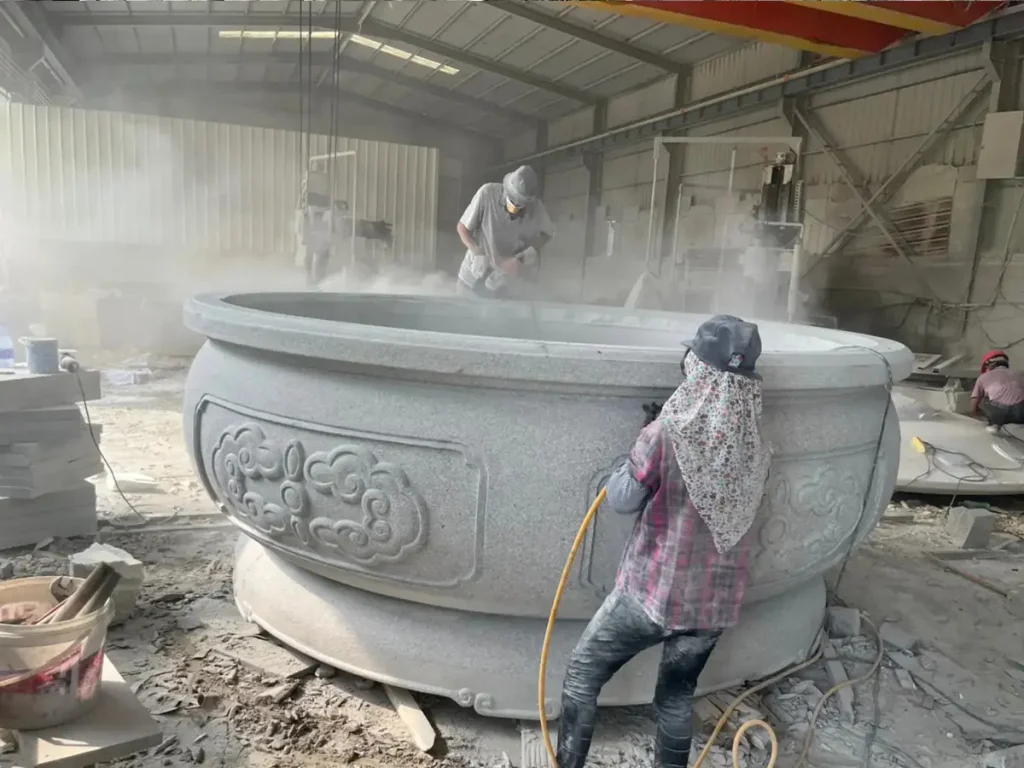 A high-scale monolithic stone planter undergoing detail carving and surface smoothing, designed for luxury commercial landscape infrastructure.