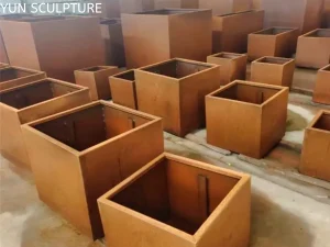 A collection of high-end custom-engineered Corten steel planters in various sizes and thicknesses, showcasing structural precision and characteristic orange-brown patina in a fabrication workshop.
