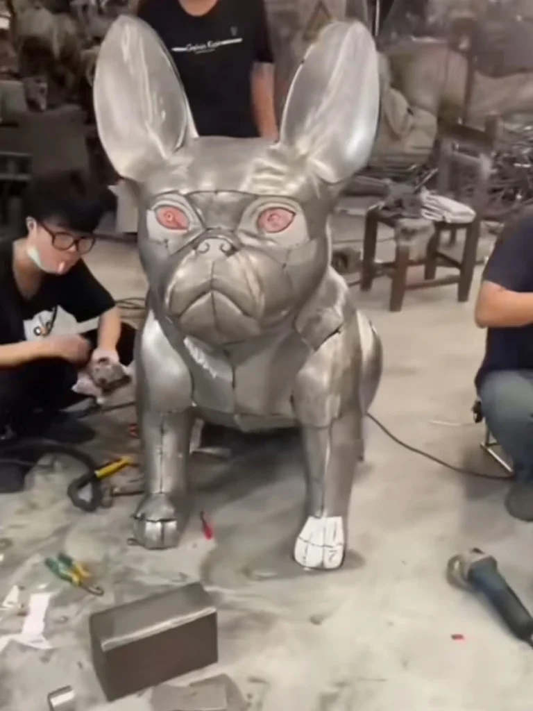 Yun Sculpture factory production scene showing the assembly of a life-size stainless steel French Bulldog, highlighting hand-welding craftsmanship.