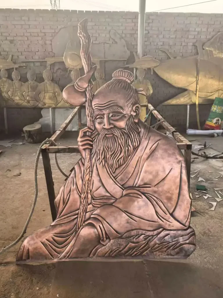A large copper relief sculpture of the sage undergoing custom metal sculpture fabrication in a metalworking shop. This meticulous crafting process highlights how raw copper is forged to exact dimensions and relief depths, ensuring the oversized artwork achieves monumental impact without overwhelming the space.