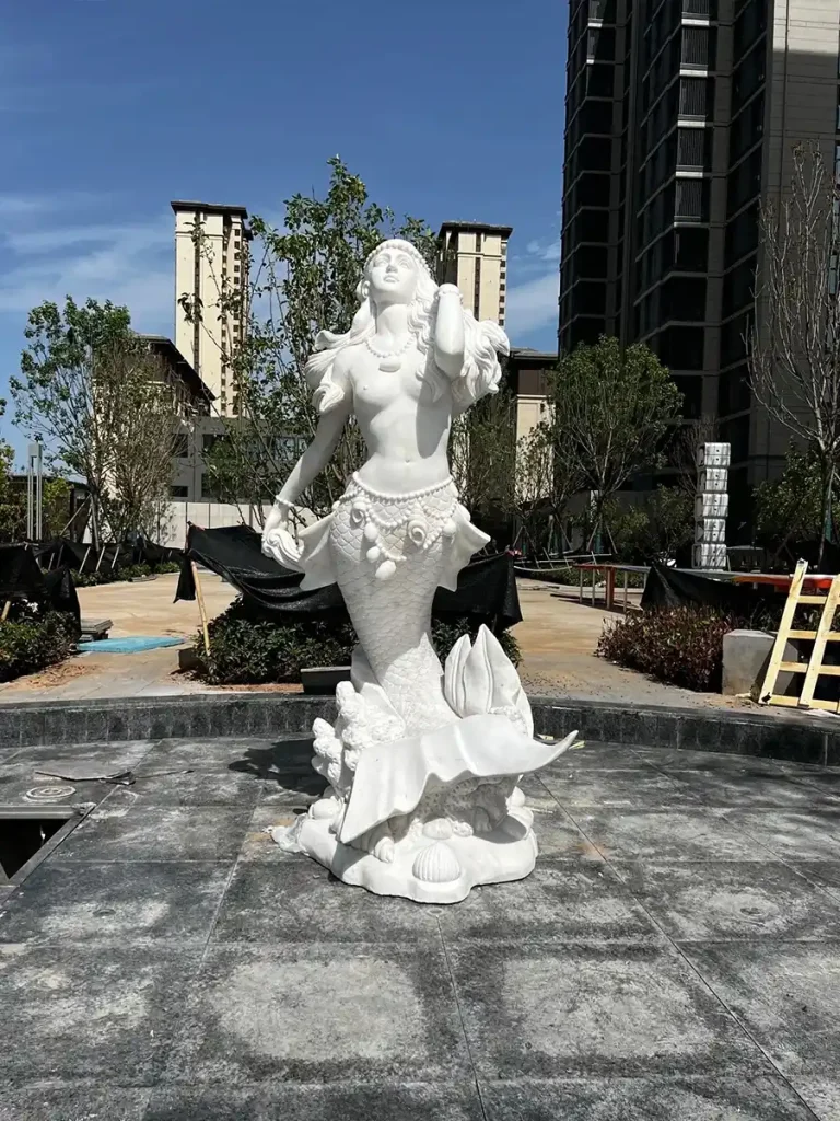 A front view of the hand-carved marble mermaid statue standing as a focal point in an outdoor pool area, showcasing elegant posture and expert craftsmanship.