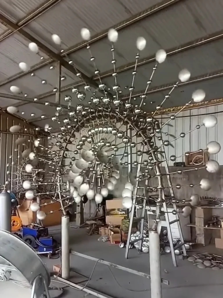A large-scale kinetic sculpture under fabrication in the factory, showcasing the complex axis and curved blade geometry that explain how these metal sculptures move with the wind without motors。