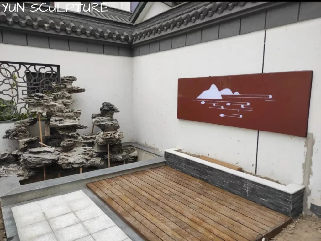 A large, heavy metal landscape wall sculpture securely installed on a white exterior stucco wall in a courtyard, demonstrating the successful result of proper substrate assessment.