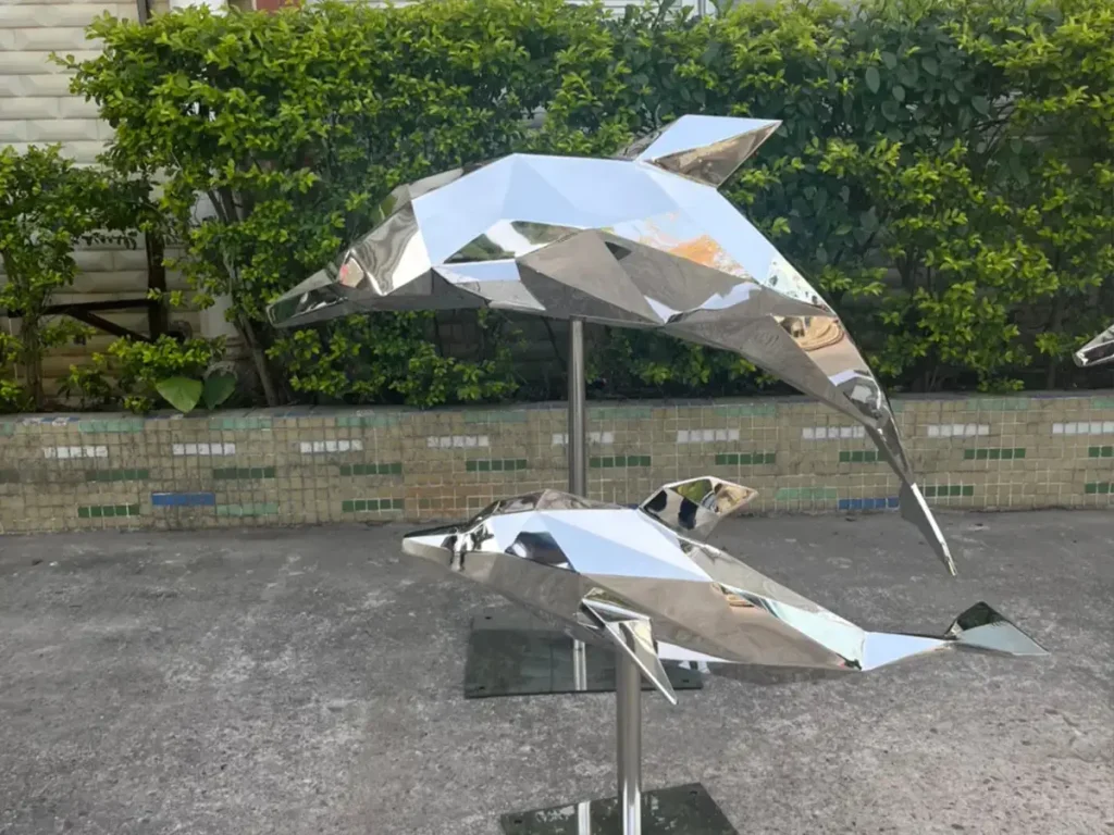 Two faceted mirror stainless steel dolphin sculptures positioned together on a single stand, highlighting modern angular metalwork.