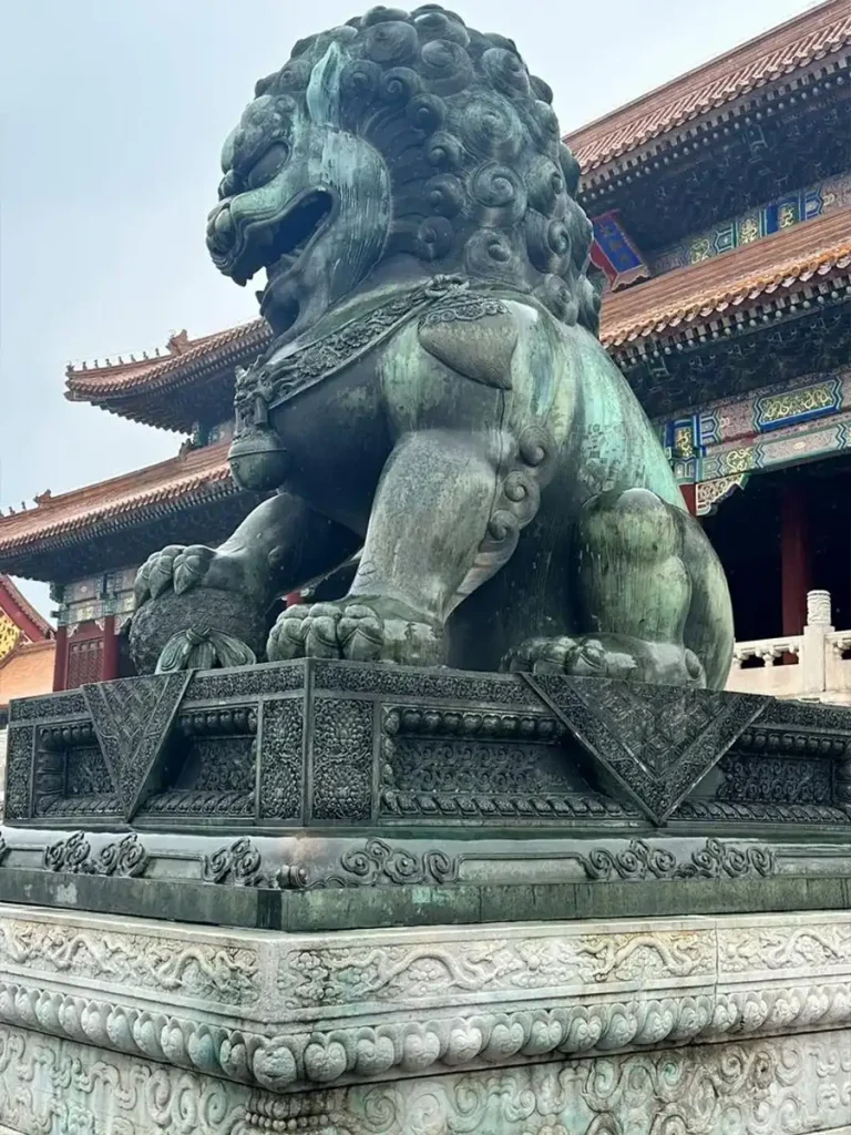 Side profile of the bronze Foo Dog at the Hall of Supreme Harmony. This angle clearly displays the prominent double-base structure, showing the detailed bronze pedestal sitting directly on the traditional carved white marble base.