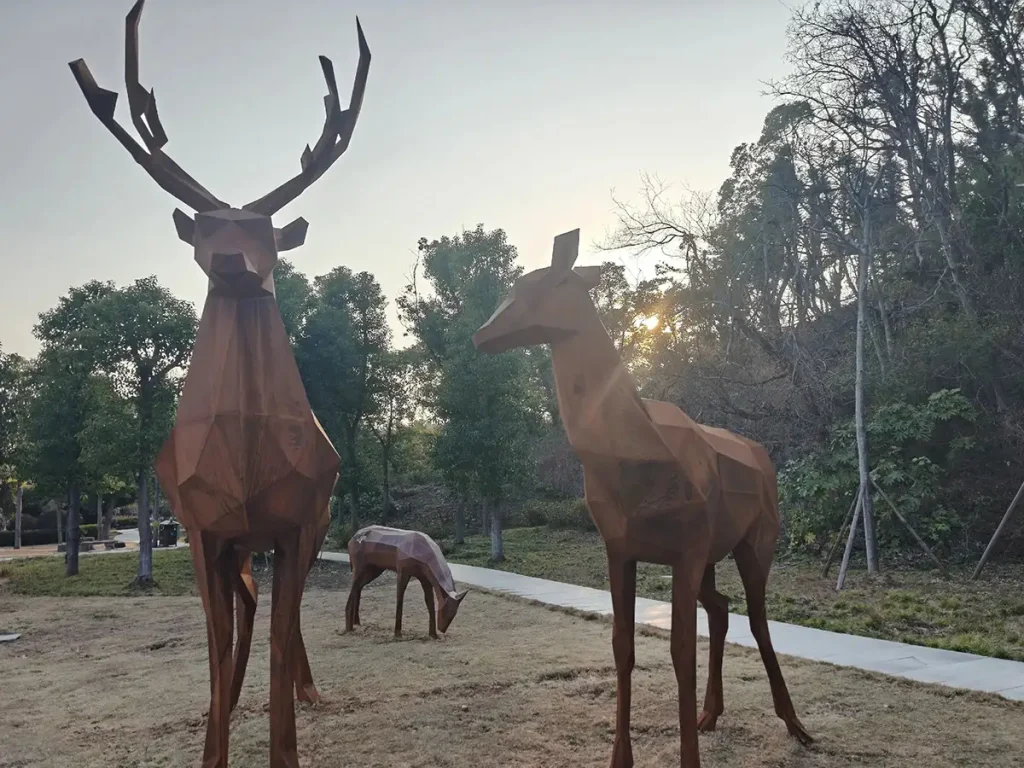 A geometric faceted Corten steel deer sculpture outdoors. Its sharp, geometric shape brings a unique aesthetic and striking visual contrast to modern gardens.