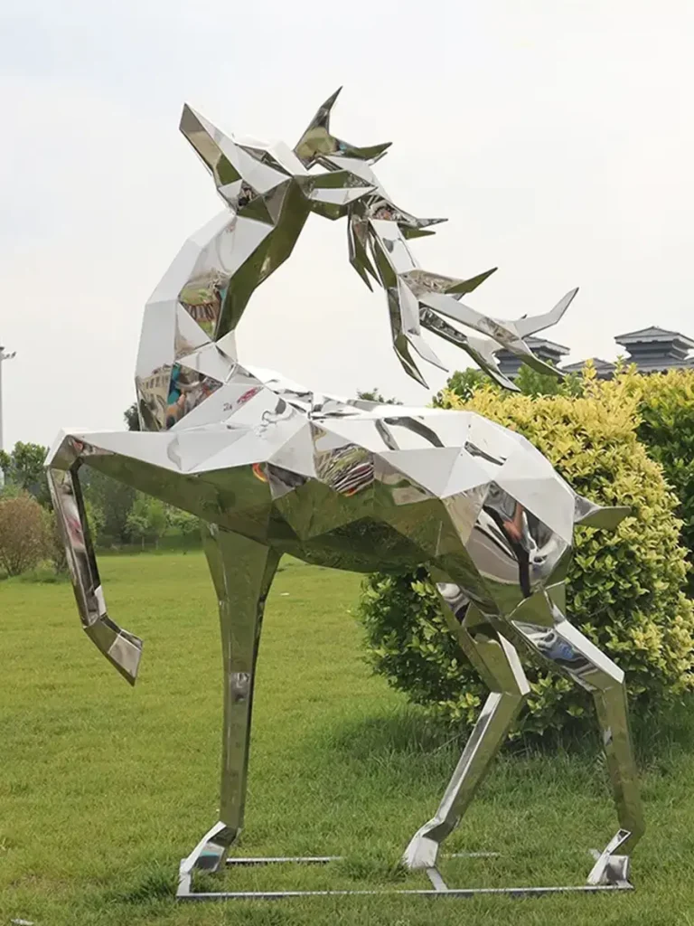 A geometric faceted mirror stainless steel deer sculpture on a lawn. It features a highly reflective surface and sharp geometric lines, perfect for modern courtyards and interacting dynamically with light.