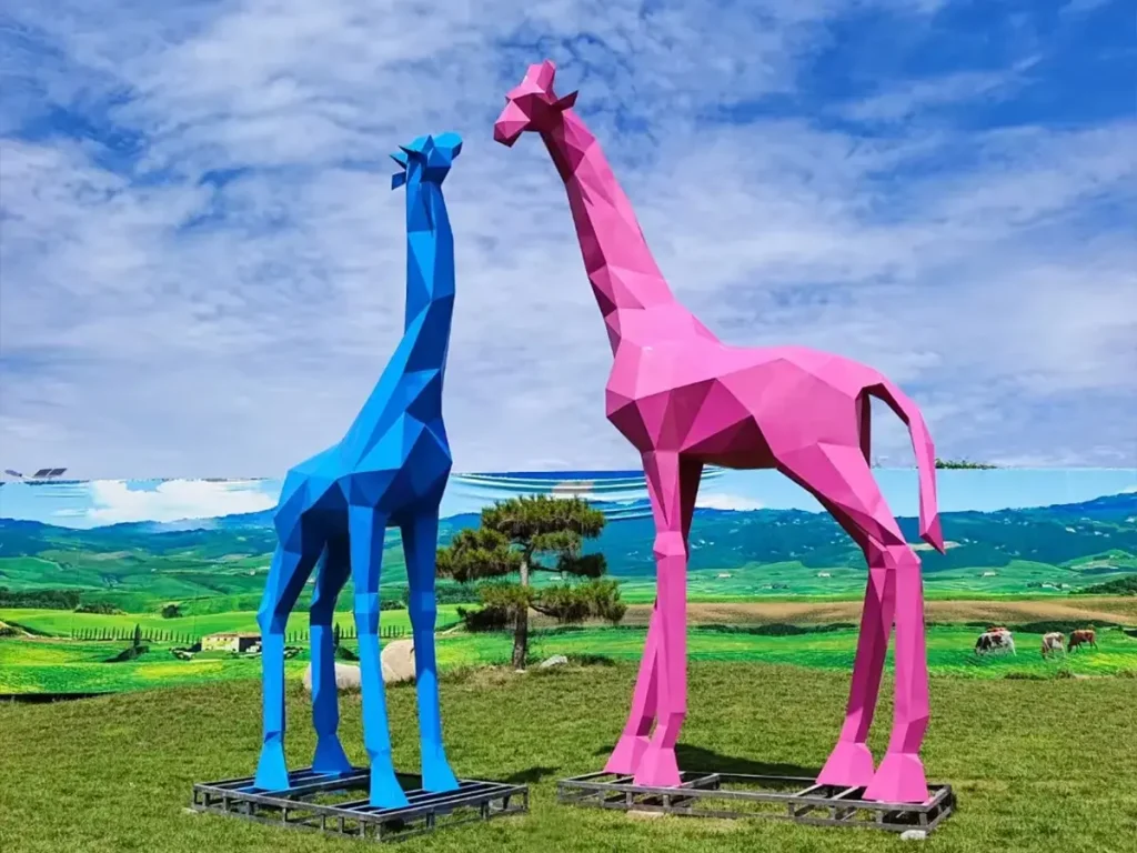 Full view of massive blue and pink faceted stainless steel giraffe statues. Crafting such five-meter-tall vertical sculptures requires treating them as architectural structures with engineered internal supports to withstand wind forces, blending artistic elegance with structural integrity.
