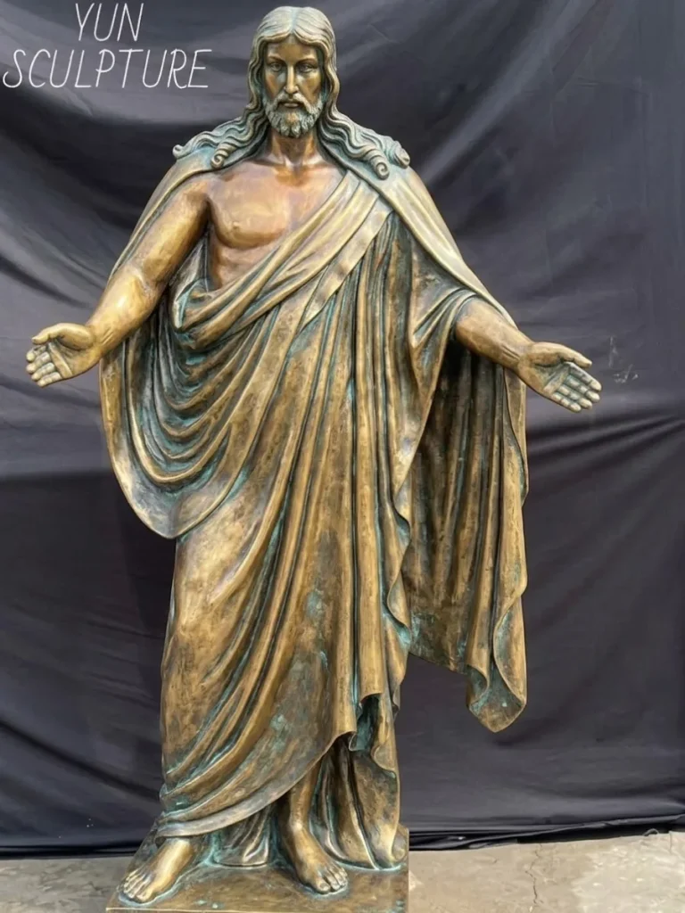 A monumental, full-length risen christ bronze statue standing in a foundry against a dark backdrop. The sculpture beautifully showcases a rich, stabilized patina—a dense layer of copper carbonate that actively resists acid rain and salt spray. This powerful visual proves why every serious outdoor bronze statue of jesus commissioned for a permanent landmark relies on this highly durable, 300+ year lifespan material.